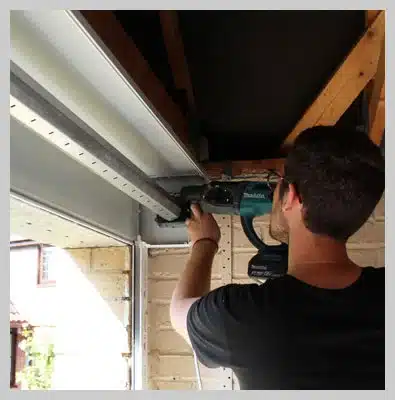 A man using a drill to install a garage door, focused on his task in a residential setting.