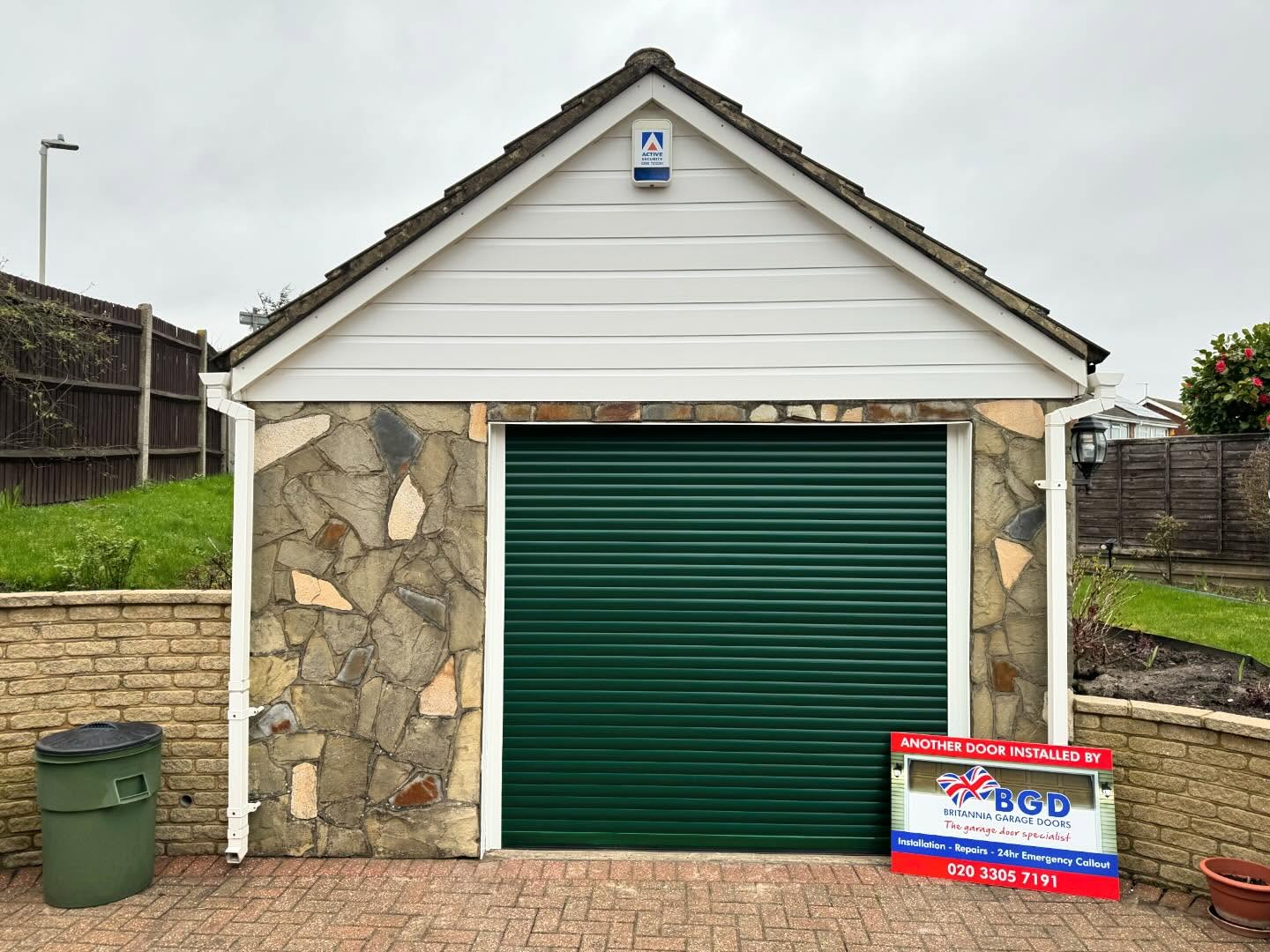 Garage with a green roller door by Britannia Garage Doors and a sign next to it.